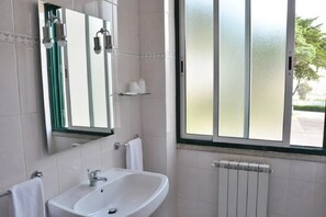 Un baño con lavamanos blanco, espejo, toallero y ventana con vidrio esmerilado.