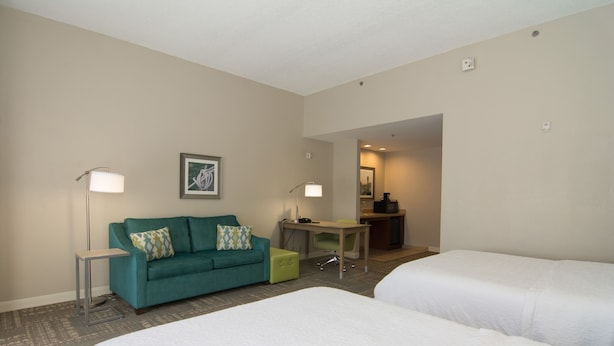Habitación de hotel con dos camas, un sofá color turquesa, un escritorio y dos lámparas de pie.