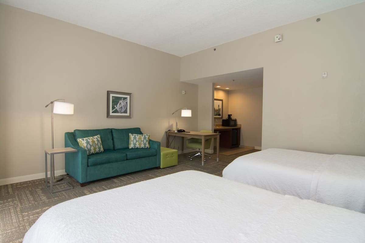 A hotel room with two beds, a teal sofa, a desk, and two floor lamps.