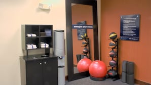 Zona de fitness con equipo de ejercicio, un tablón de anuncios y un cartel que promociona energía.