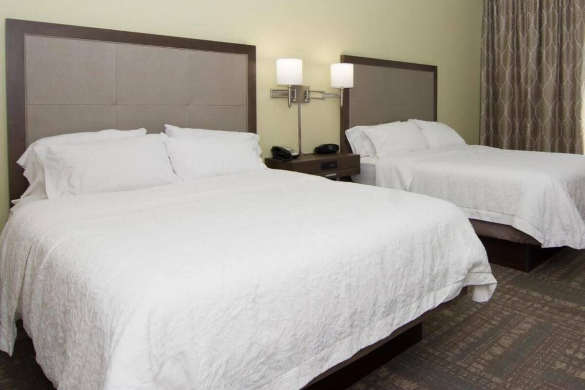 A hotel room with two beds, a nightstand with a phone, and a lamp.
