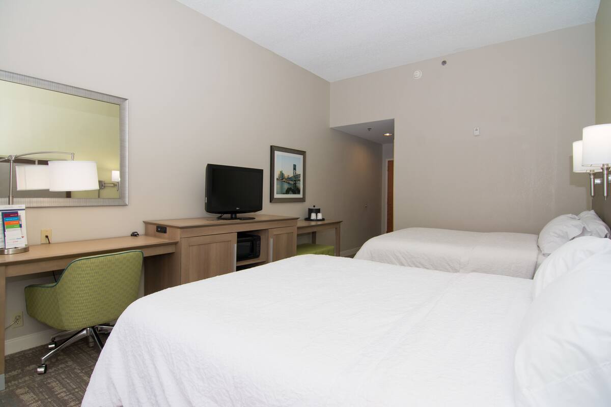 A hotel room with two beds, a desk with a computer and a television, a chair, and a large mirror.