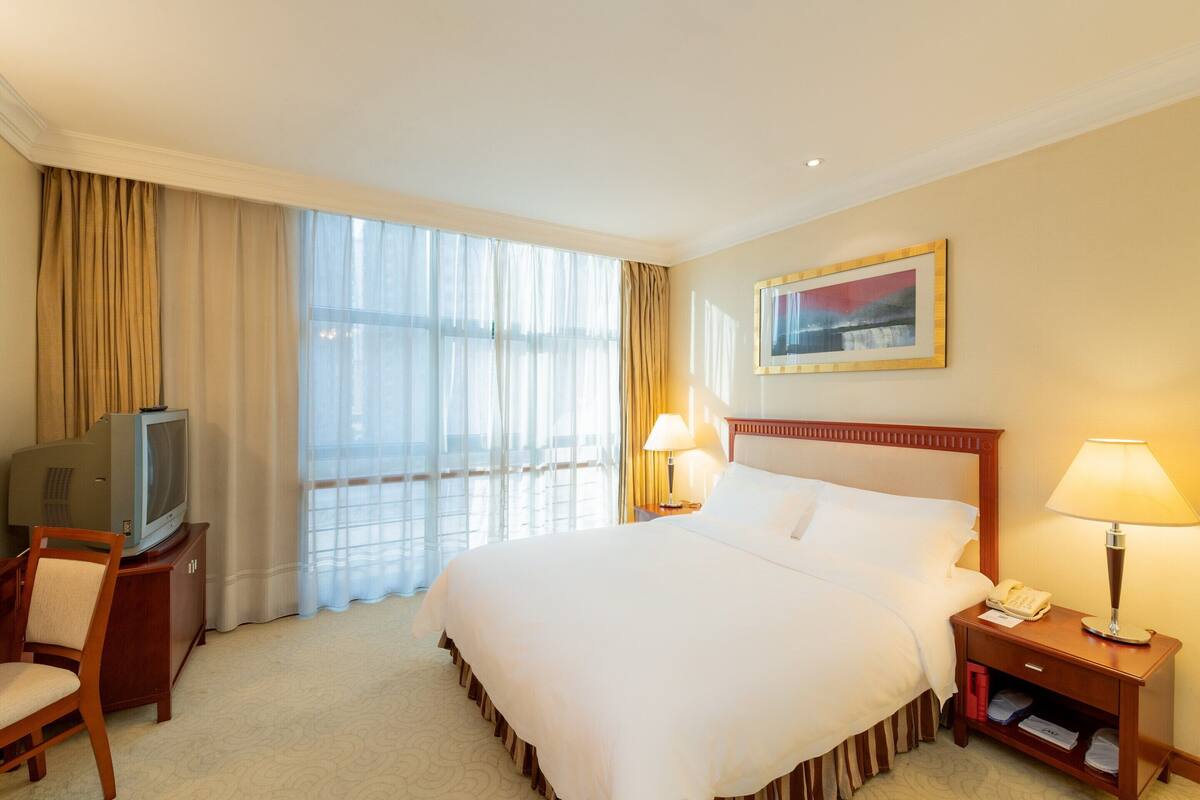 A hotel room with a large bed, a television on a wooden cabinet, two bedside lamps, and a window with curtains.