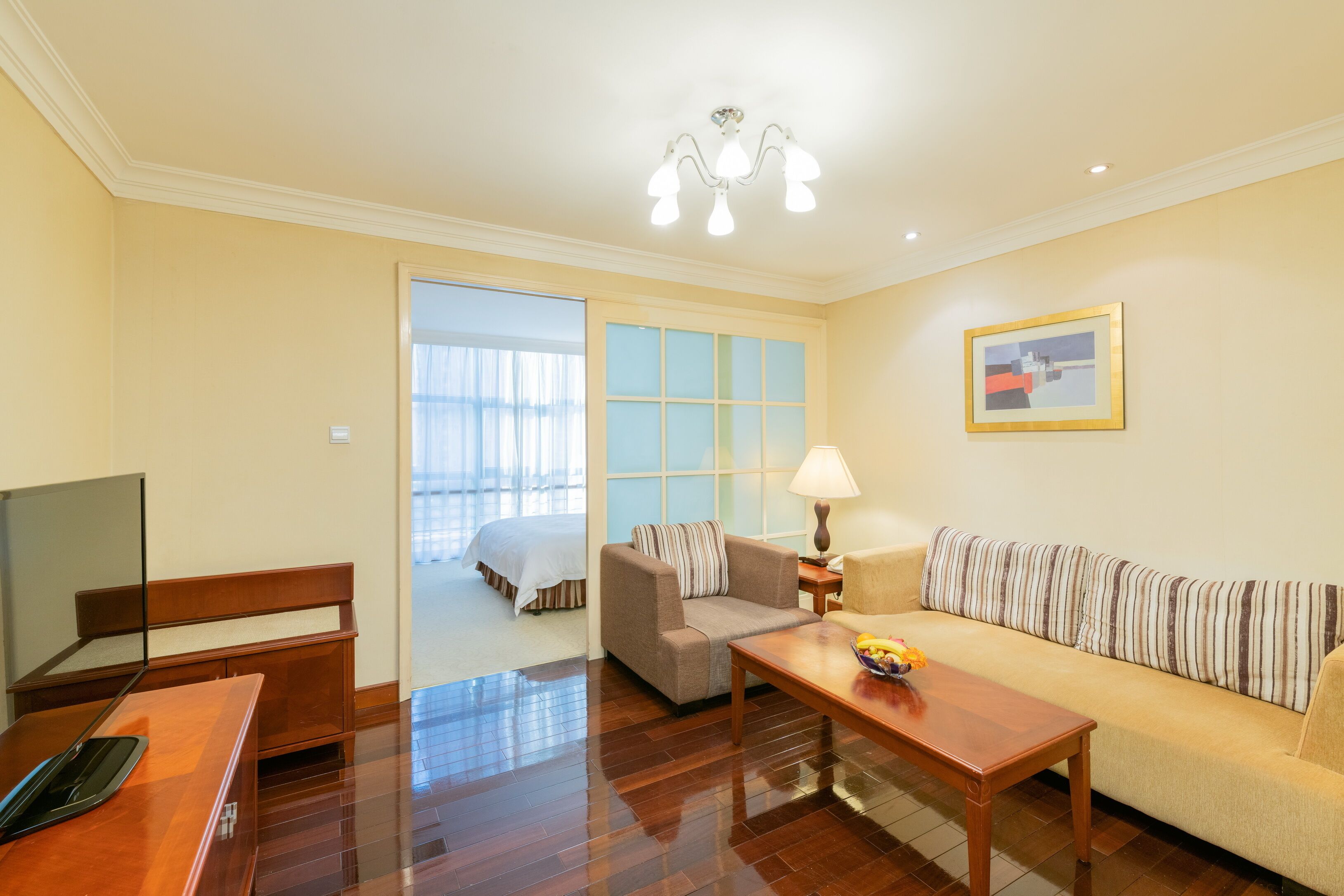 A hotel room with a wooden desk, a sofa, a TV, and a bed.