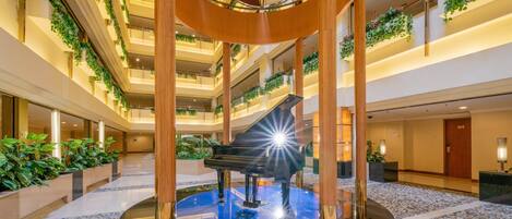 A hotel atrium with a grand piano at the center, surrounded by multiple floors with balconies adorned with greenery.