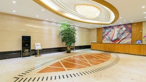 A lobby with a large chandelier, a reception desk, a digital information kiosk, and a large abstract painting on the wall.