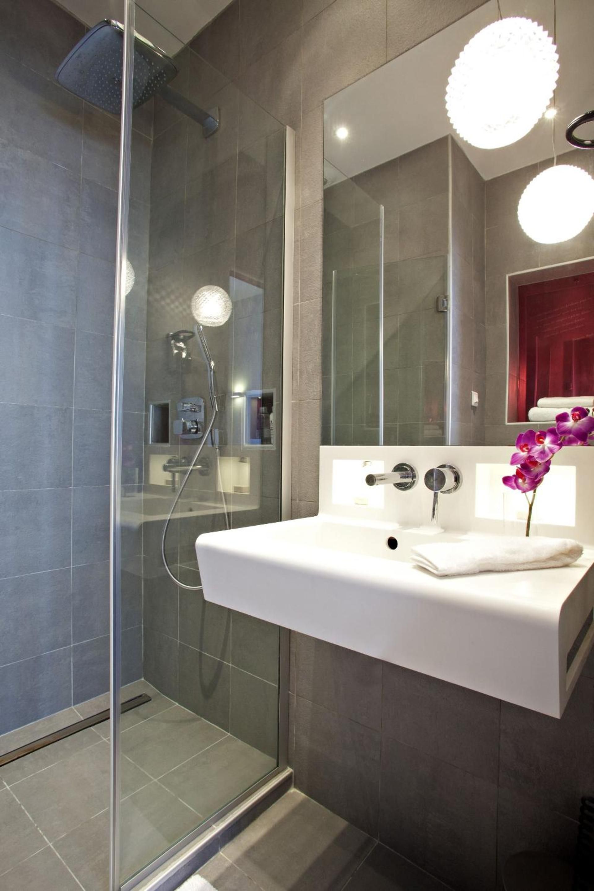 A modern bathroom with a glass-enclosed shower, a white sink, and a large mirror with two round lights.