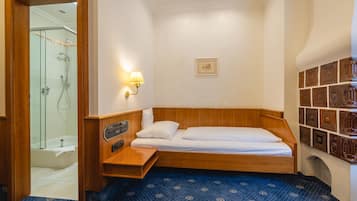 A compact room with a wooden bed, a small bedside table, a wall-mounted light, and a shower area.