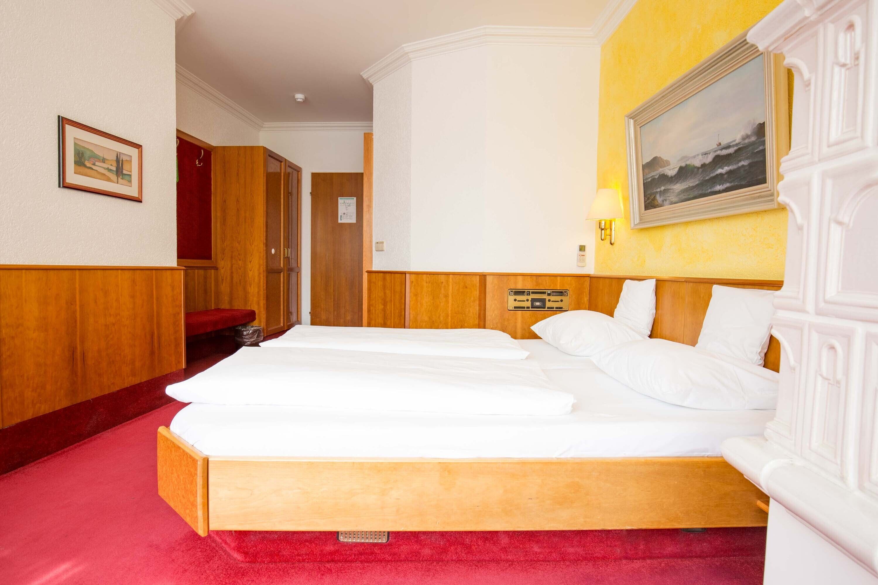 A hotel room with a large bed, wooden headboard, and a red carpet.