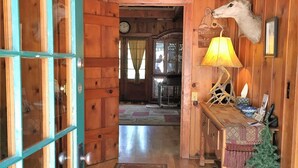 Un interior de madera con un vidrio, una alfombra, una lámpara y la cabeza de un ciervo montada en la pared.