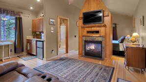 Una sala de estar acogedora con chimenea, techo de madera y un televisor de pantalla plana montado en la pared.