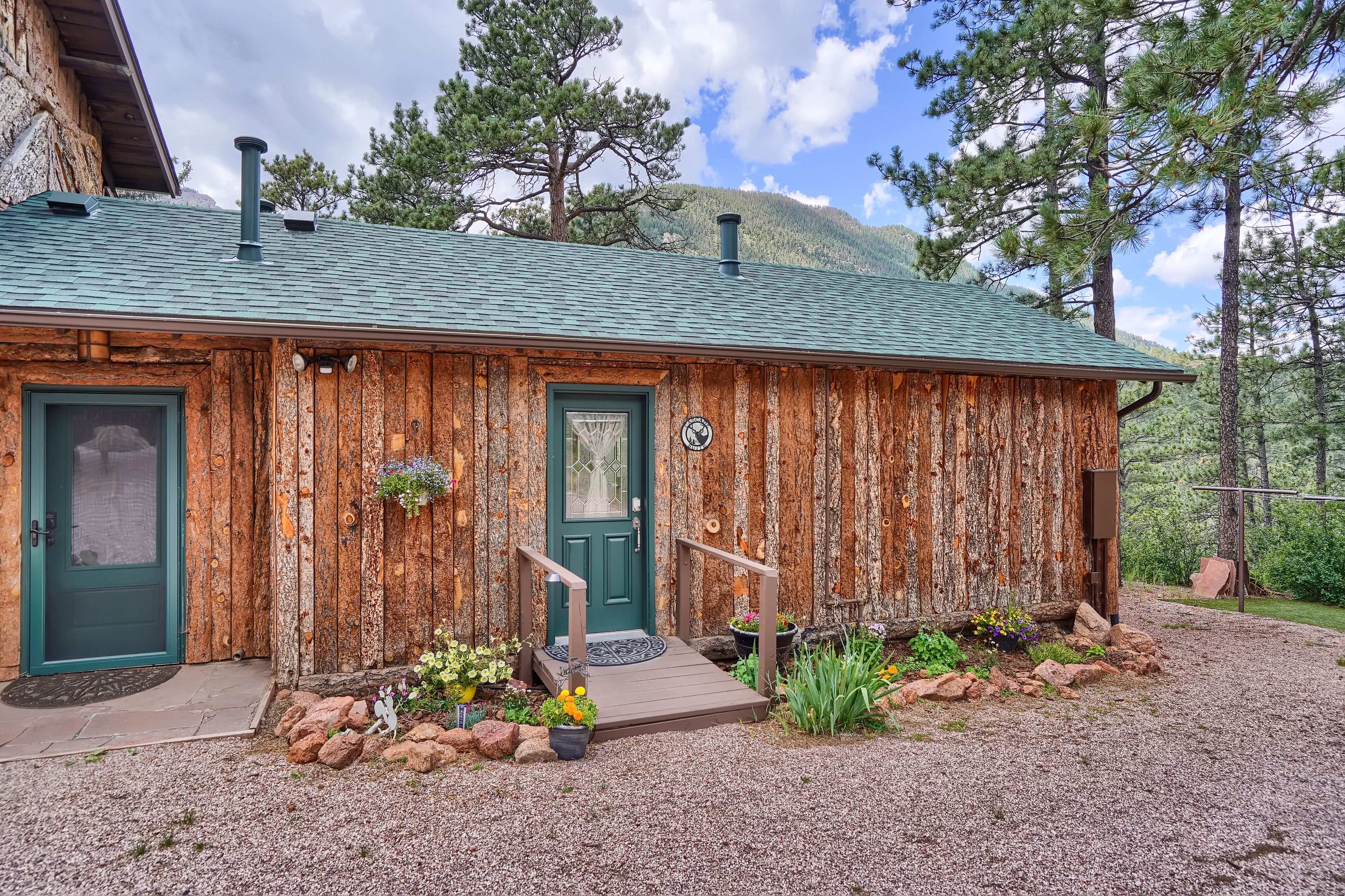 A rustic wooden cabin with a green door, a small porch, and a stone pathway leading to the entrance.
