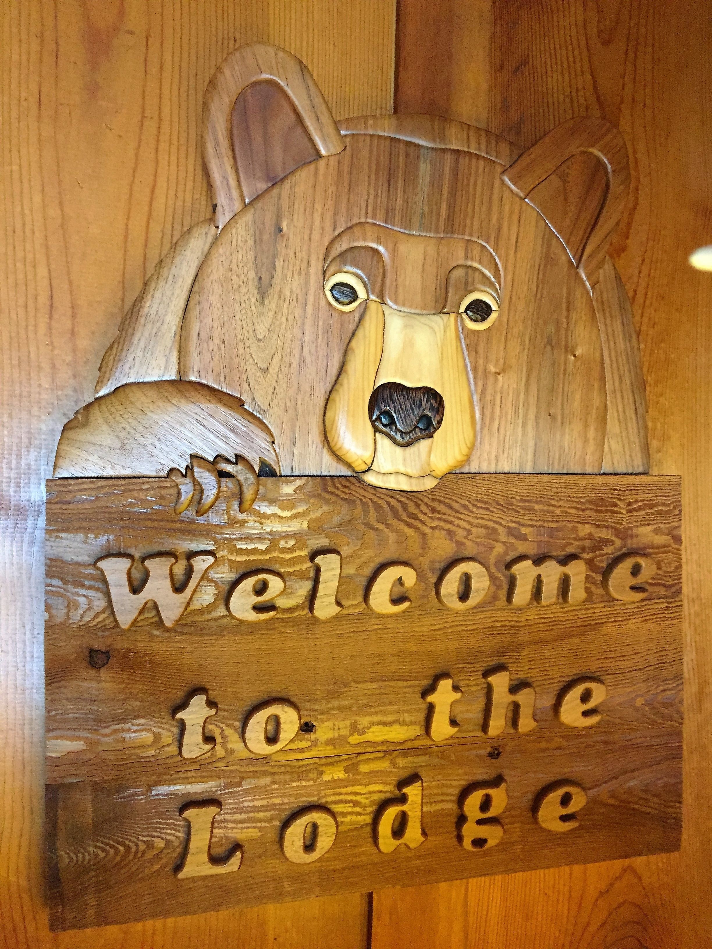 Een houten bord met het gezicht van een beer en de tekst 'Welcome to the Lodge'.