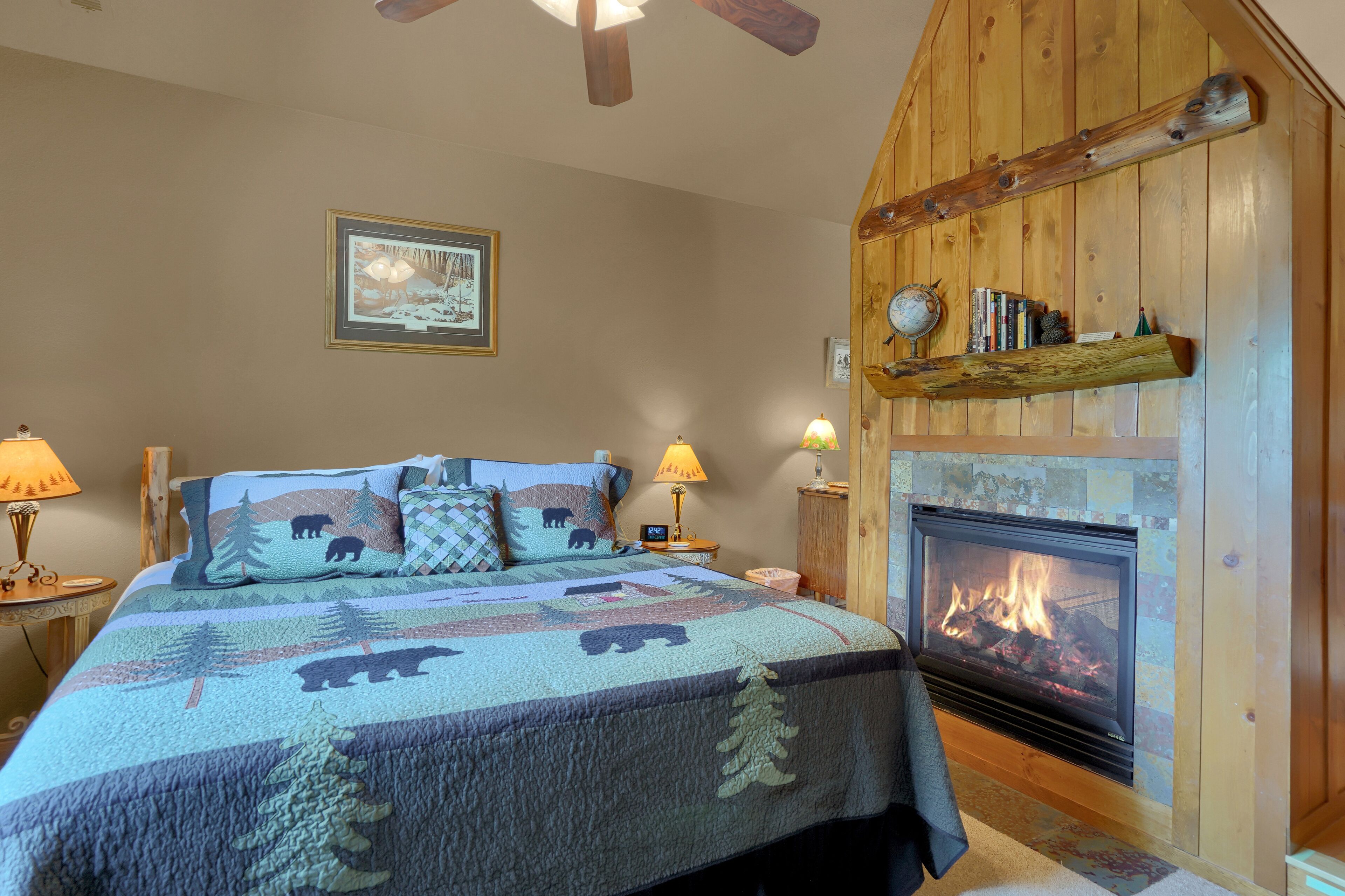 A cozy bedroom with a large bed, a fireplace, and a wooden ceiling.