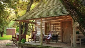 A rustic log cabin with a porch, rocking chairs, and a small table.
