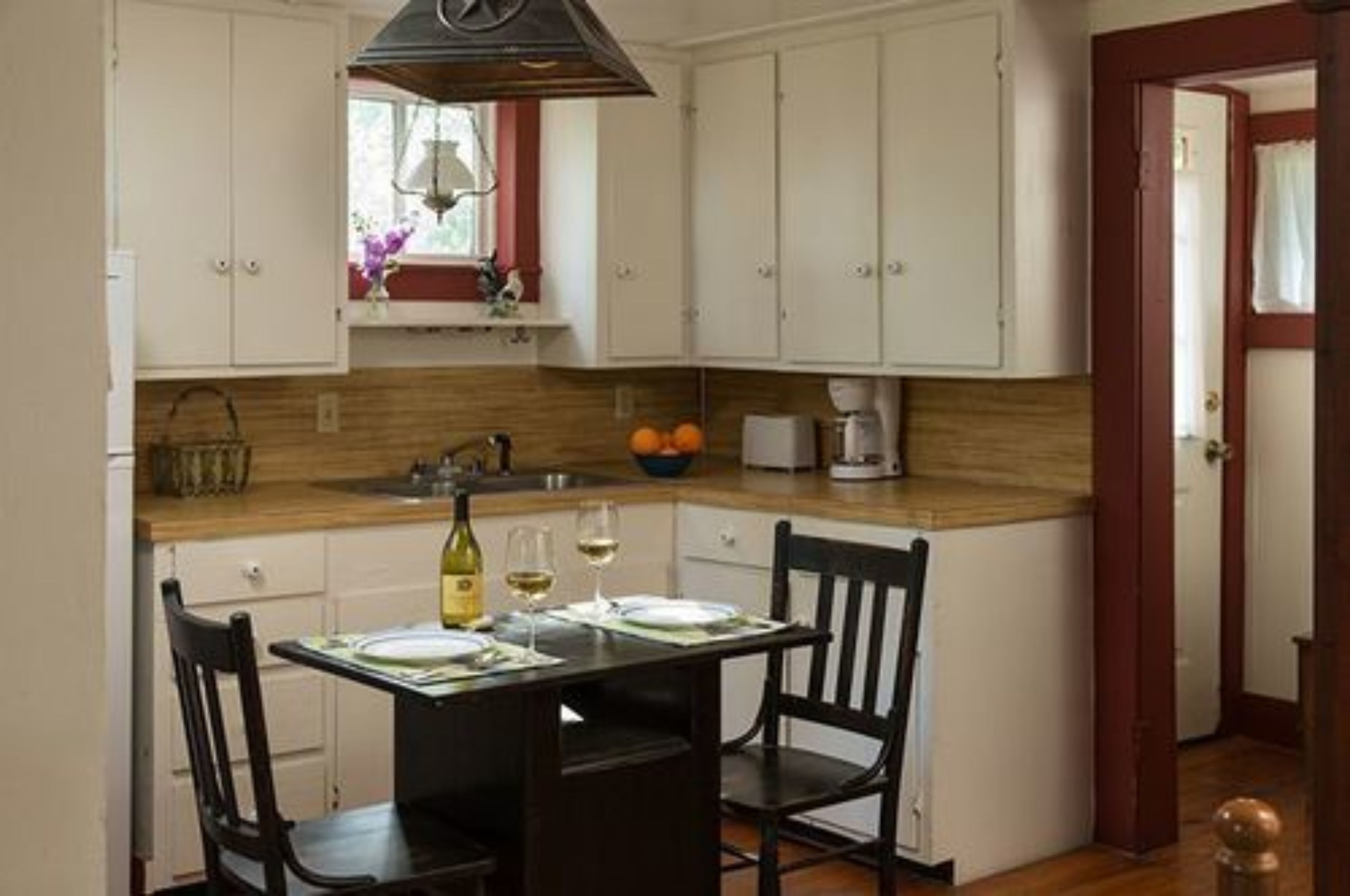 A kitchen with white cabinets, a wooden countertop, a dining table with chairs, and a window with a view of the outdoors.