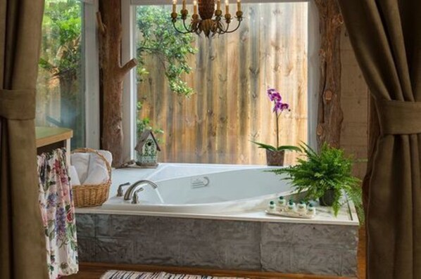 A bathroom with a large bathtub, wooden window frames, and a chandelier. - BlissWood B&B Ranch (Cat Spring)