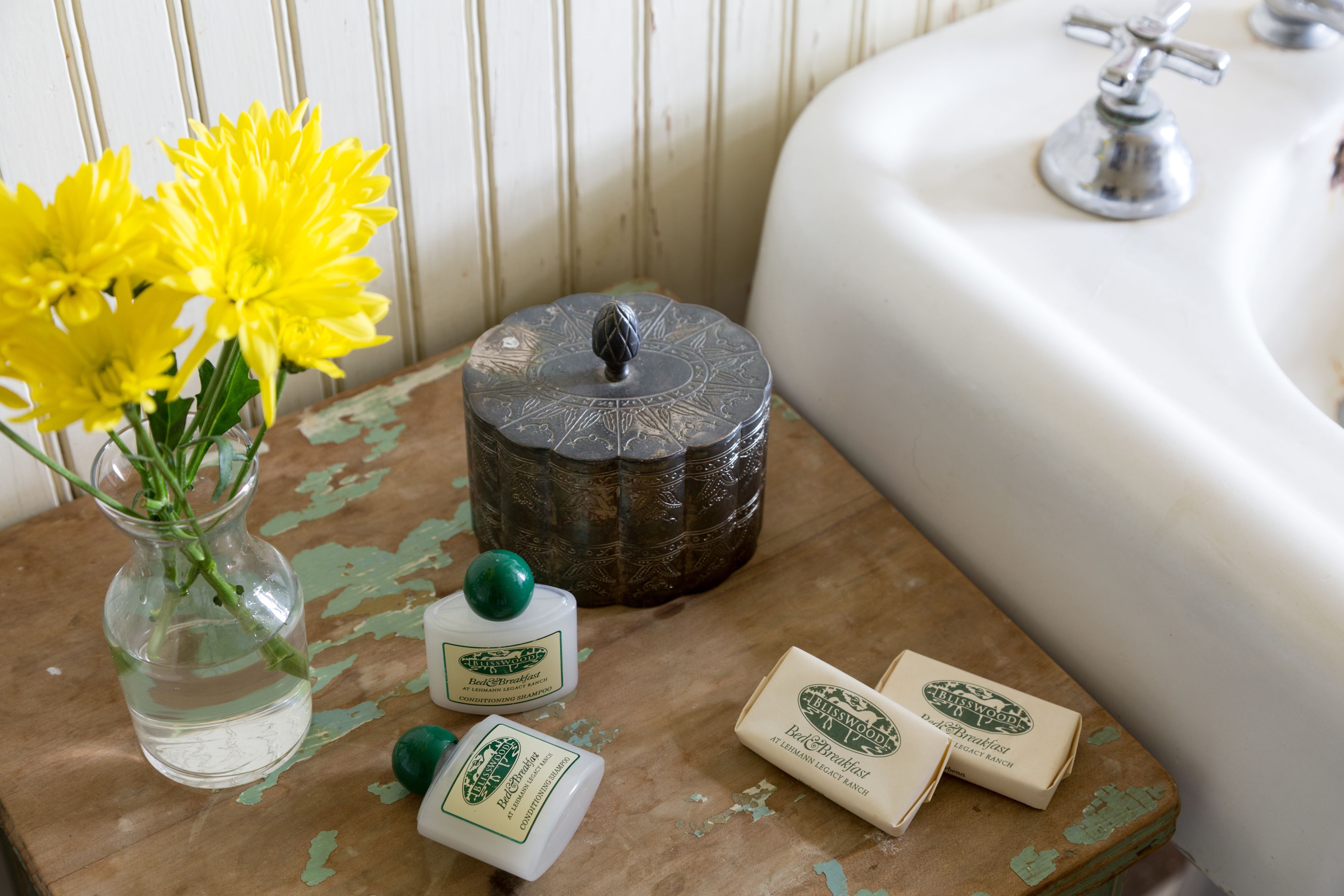 Un meuble-lavabo de salle de bain avec un évier blanc, un pot décoratif et un vase contenant des fleurs jaunes.