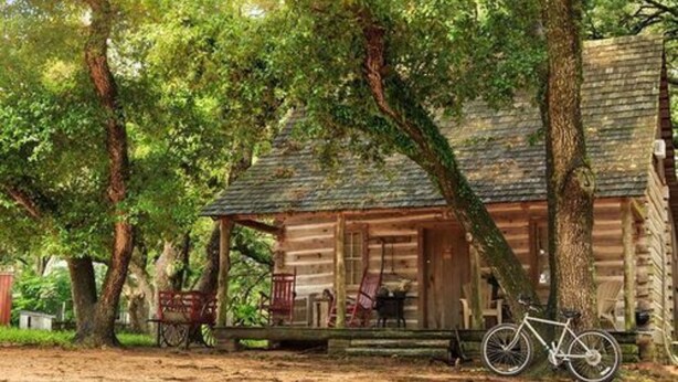 A rustic log cabin with a porch, surrounded by trees.