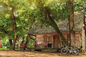 A rustic log cabin with a porch, surrounded by trees. - BlissWood B&B Ranch (Cat Spring)