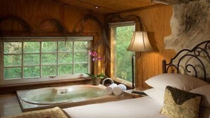 A bedroom with a large window, a bathtub, and a bed with pillows.