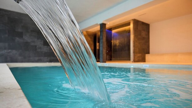 A pool with a waterfall feature, indoor lighting, and a stone wall in the background. - Canyamel Classic & Spa, solo Adultos (Capdepera)