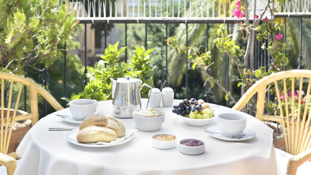 A round table with a white tablecloth, set with breakfast items including bread, fruits, and condiments. - Adrian Hotel (Athens)