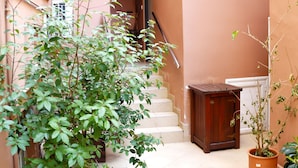 A narrow alleyway with a wooden planter and potted plants, a staircase leading to a door, and a small window on the building. - Adrian Hotel (Athens)