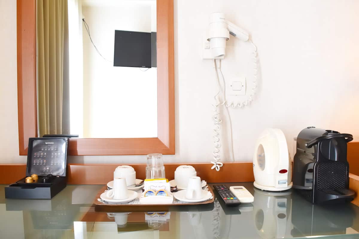 A hotel room with a glass table, a coffee maker, a kettle, a phone, and a calendar.
