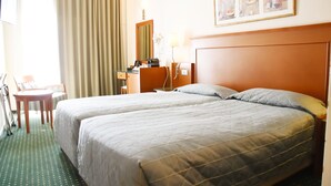 A hotel room with two beds, a desk, a chair, a lamp, and a framed picture on the wall. - Adrian Hotel (Athens)