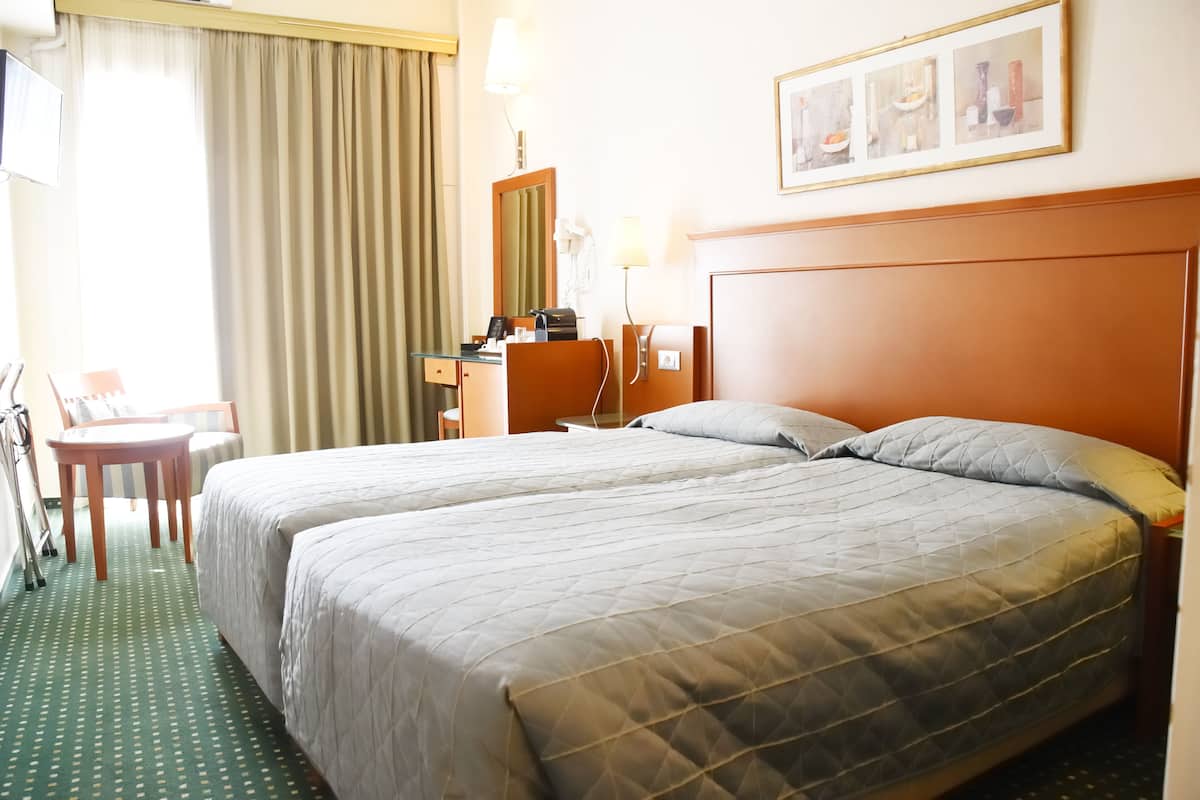 A hotel room with two beds, a desk, a chair, a lamp, and a framed picture on the wall.