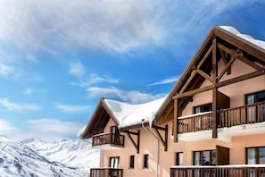 Un immeuble à plusieurs étages doté de balcons, se dressant sur fond de montagnes enneigées.