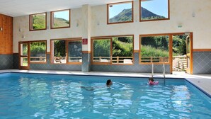Ein Hallenbad mit großen Fenstern, einer Holzterrasse und Blick auf eine Berglandschaft.