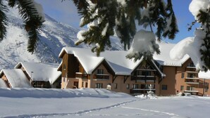 Ein schneebedecktes Chalet mit mehreren Gebäuden, darunter ein Hauptgebäude mit Balkonen und kleinere Blockhäuser.