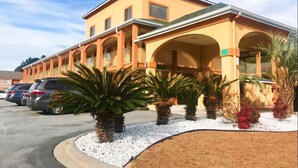 A hotel with a two-story structure, multiple balconies, and a parking lot with several cars.
