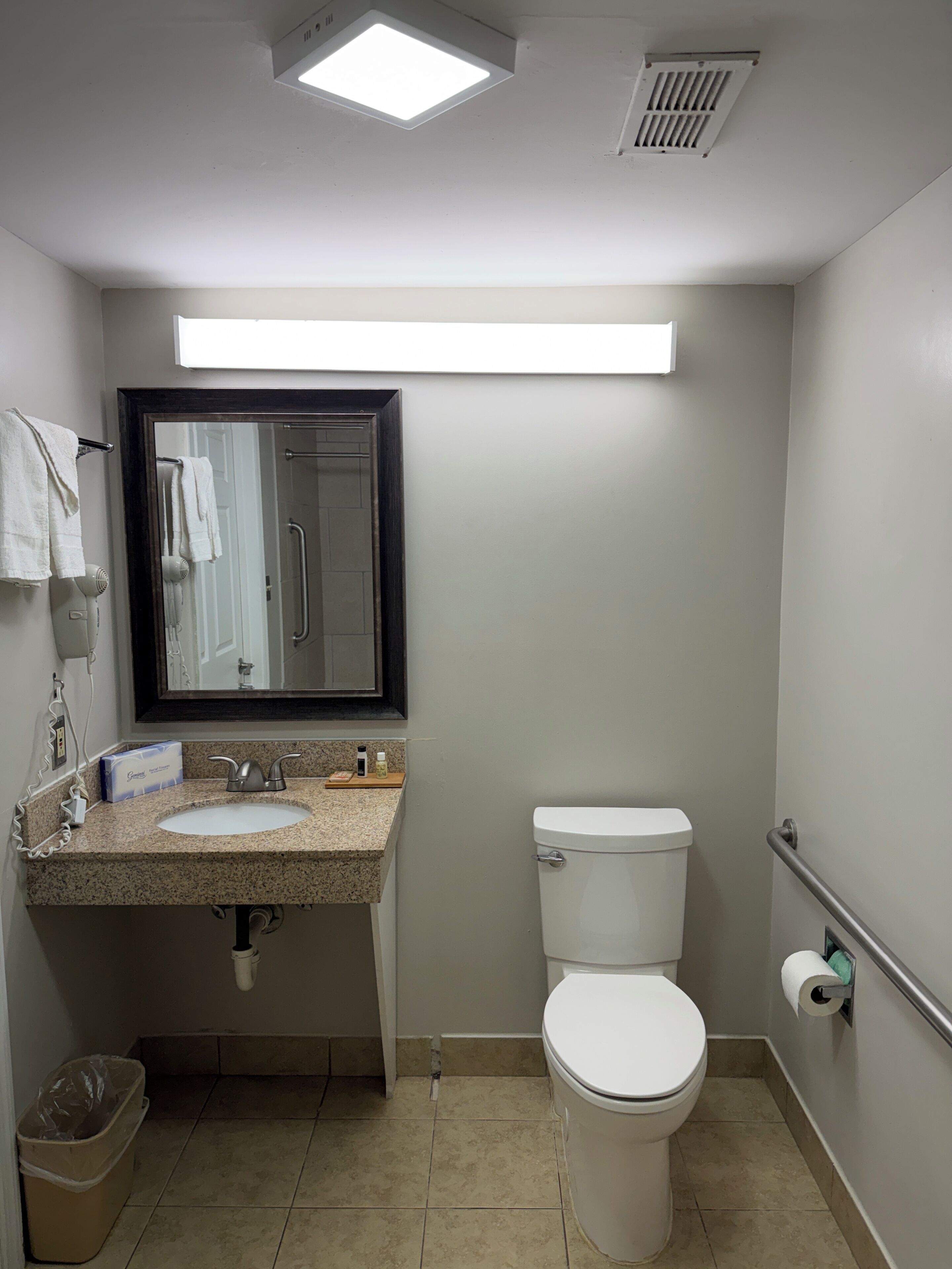 A small, clean bathroom with a sink, mirror, toilet, and a trash bin.