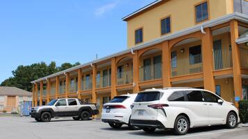 Un hôtel à étages, doté de balcons et d’un parking où sont stationnés plusieurs véhicules.