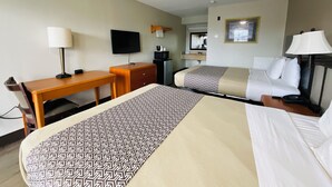 A hotel room with a bed, a desk, a chair, a TV, a mirror, and a bedside table with a lamp.
