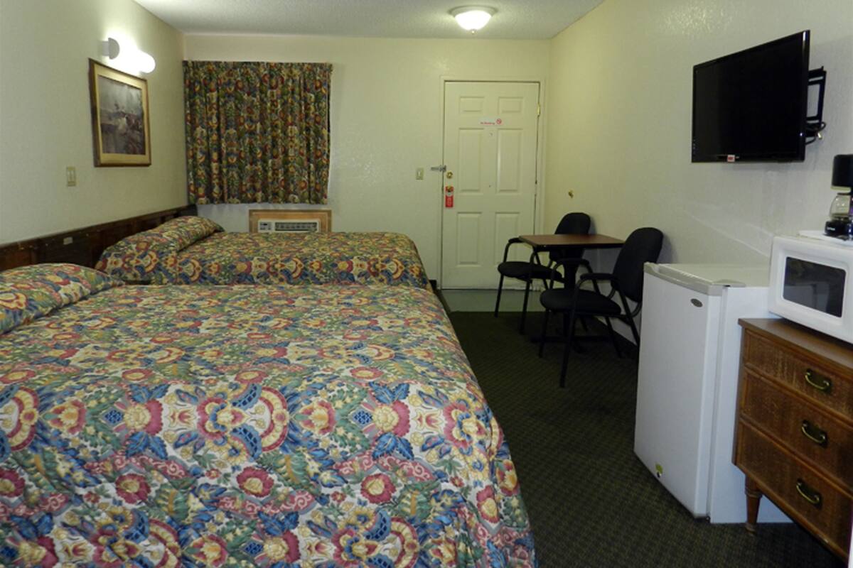A hotel room with two beds, a desk, a chair, a television, and a microwave.
