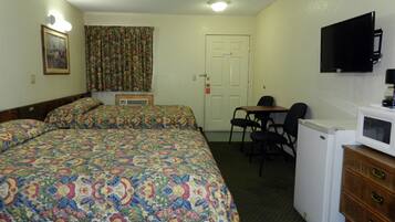 Quarto de hotel com duas camas, uma mesa, uma cadeira, televisão e micro-ondas.