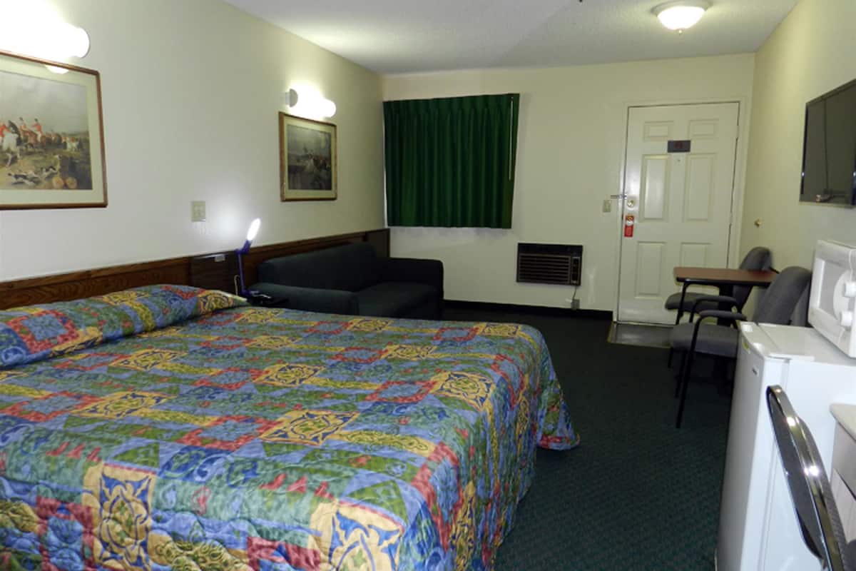 A hotel room with a large bed, a desk, a chair, a television, and a door.