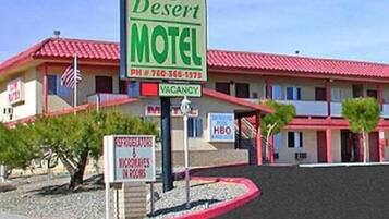 Een motel genaamd 'High Desert Motel' met een rood dak en een bord dat aangeeft dat er een kamer vrij is.