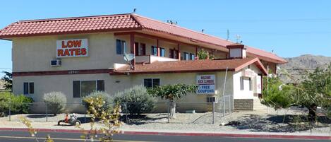 A motel with a red-tiled roof, a sign advertising low rates, and a welcome sign for rock climbers.