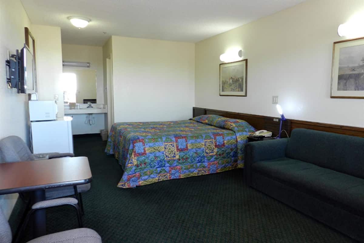 A hotel room with a bed, a couch, a desk, and a kitchenette.