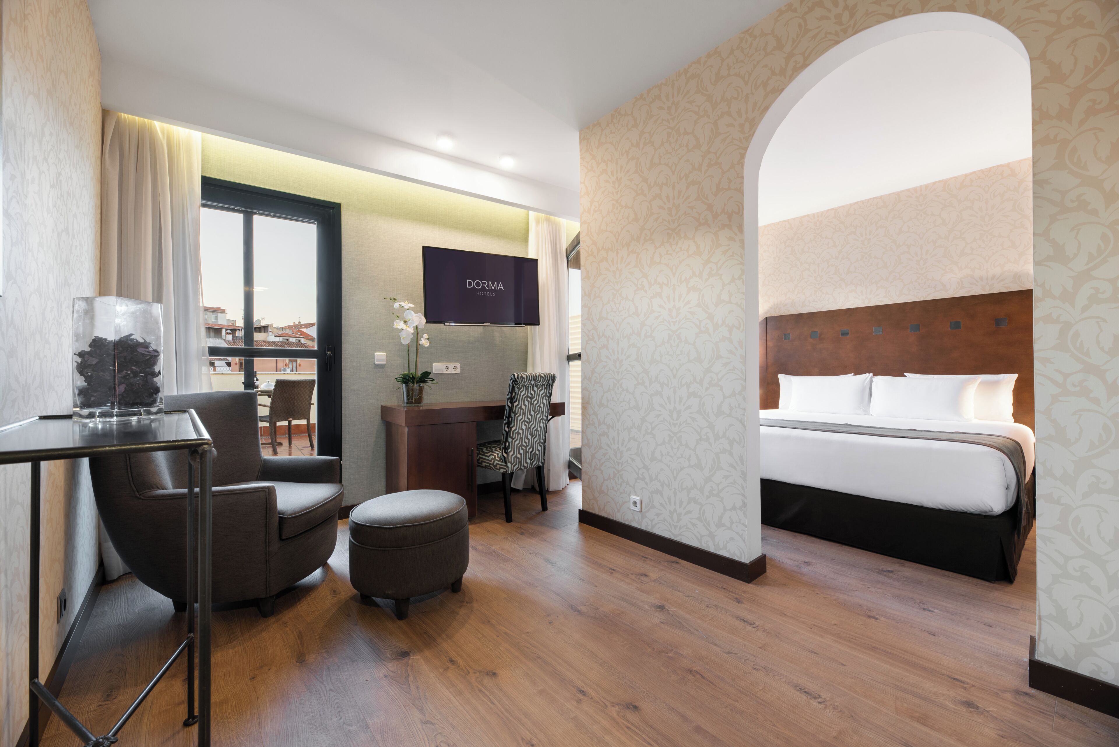 Ein Hotelzimmer mit Bett, Schreibtisch, Sessel, Fernseher und Blick auf die Stadt.