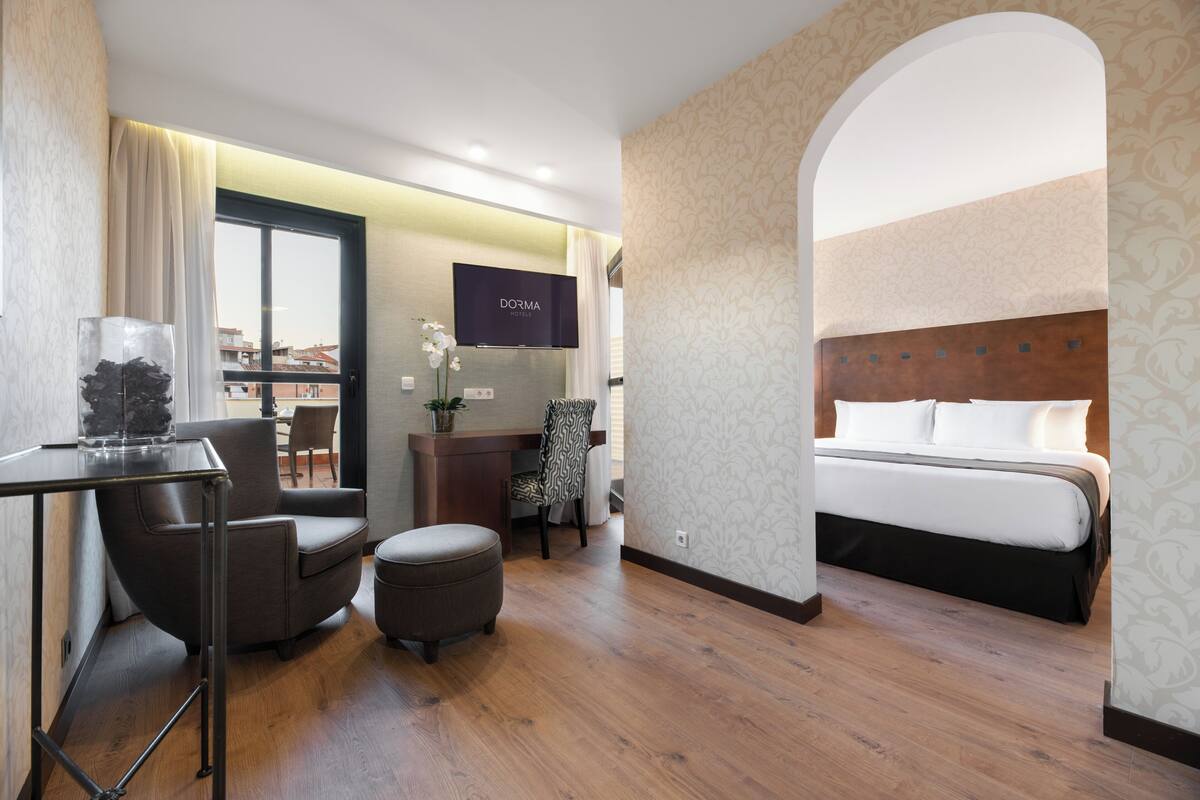 Ein Hotelzimmer mit Bett, Schreibtisch, Sessel, Fernseher und Blick auf die Stadt.