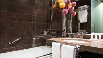 A modern bathroom with a glass shower enclosure, a wooden vanity with a sink, and a vase of flowers.
