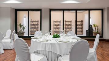 Un salón de conferencias con mesas redondas, sillas blancas y un amplio ventanal con vistas a estanterías.
