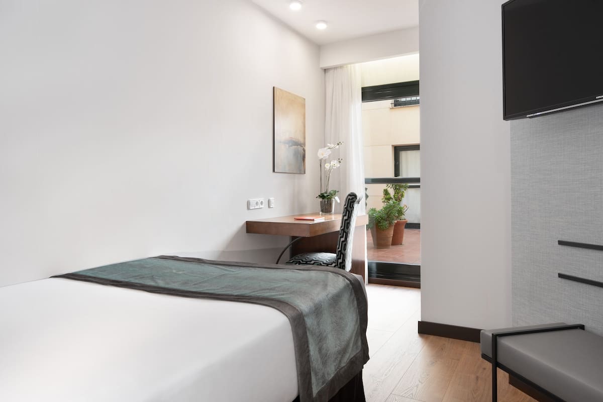 A modern hotel room with a bed, a desk, a chair, a flat-screen TV, and a potted plant.