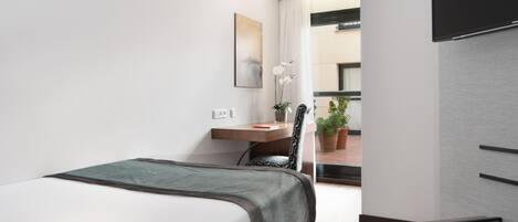 Une chambre d’hôtel moderne équipée d’un lit, d’un bureau, d’une chaise, d’un téléviseur à écran plat et d’une plante en pot.